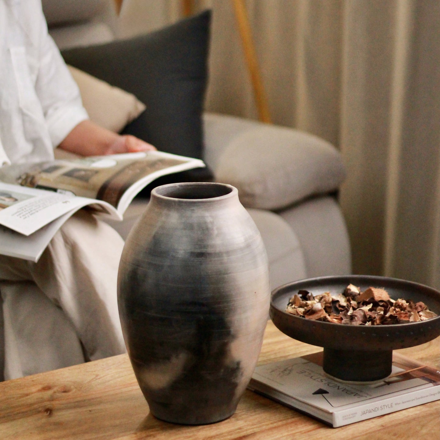 Kaari vase and set on a table with a person reading a magazine on the background
