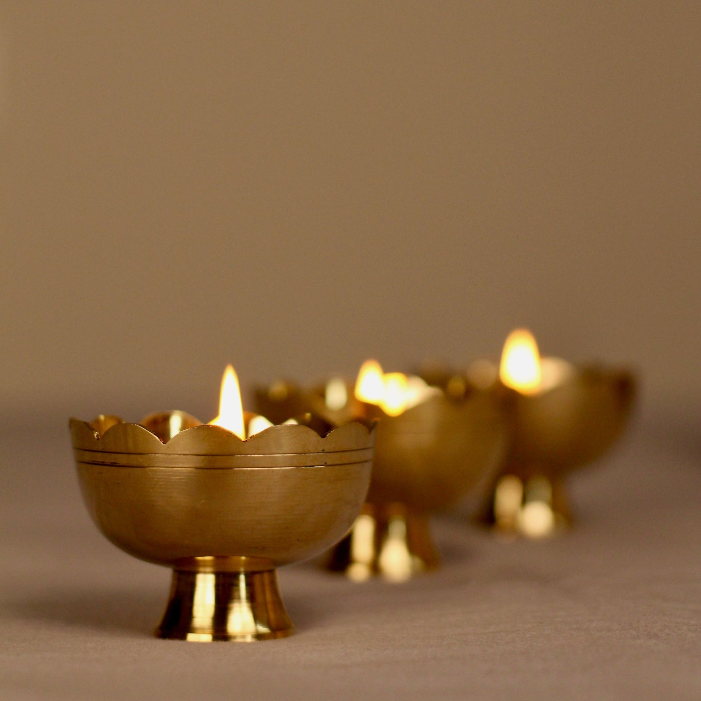 Three brass candle holders with lit candles on a neutral background
