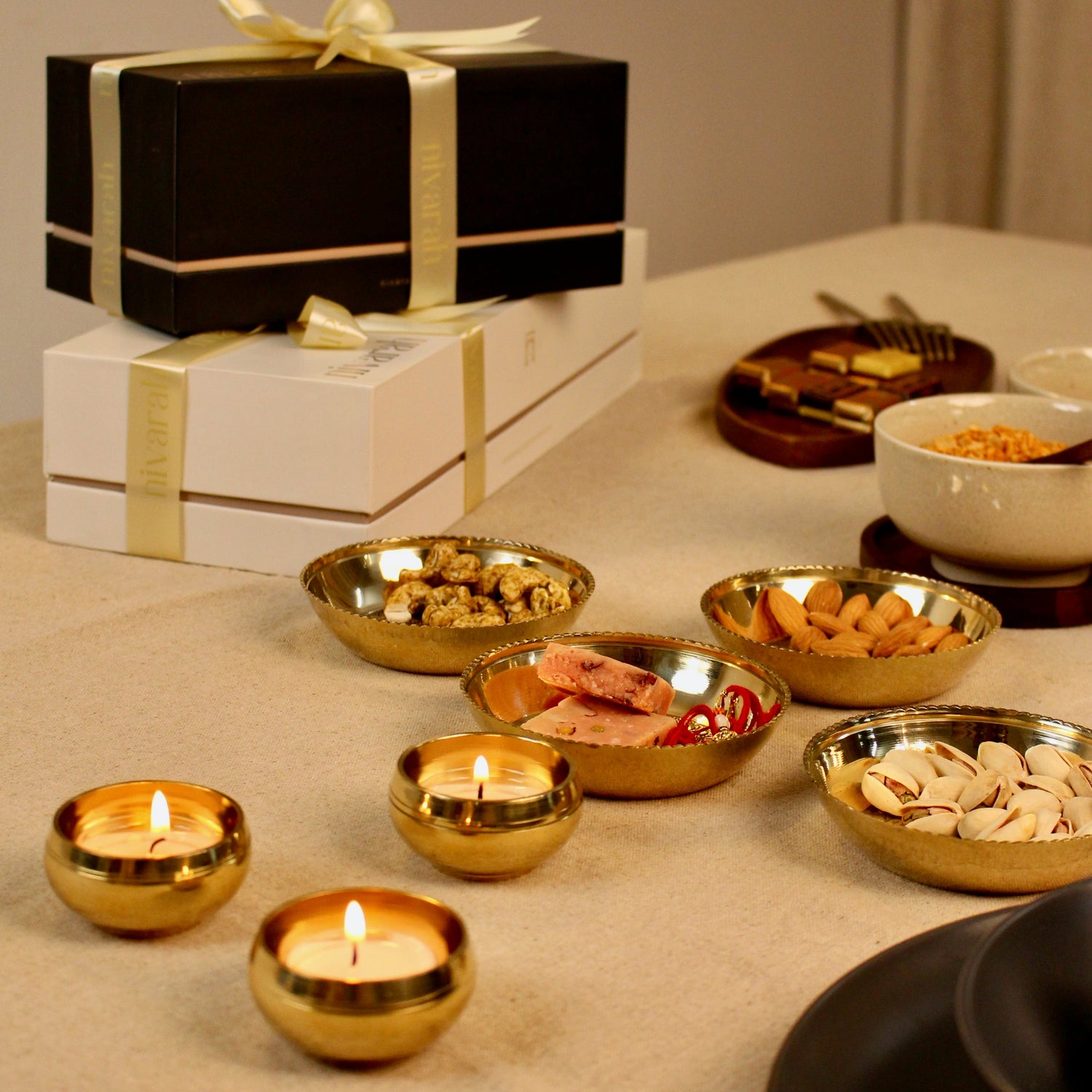 Dining table setting with brass tealight holders, candles, and a gift box.