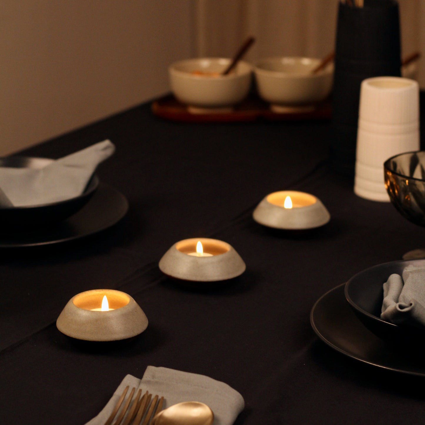 Dining table setting with candles, plates, and cutlery in a warm ambiance.