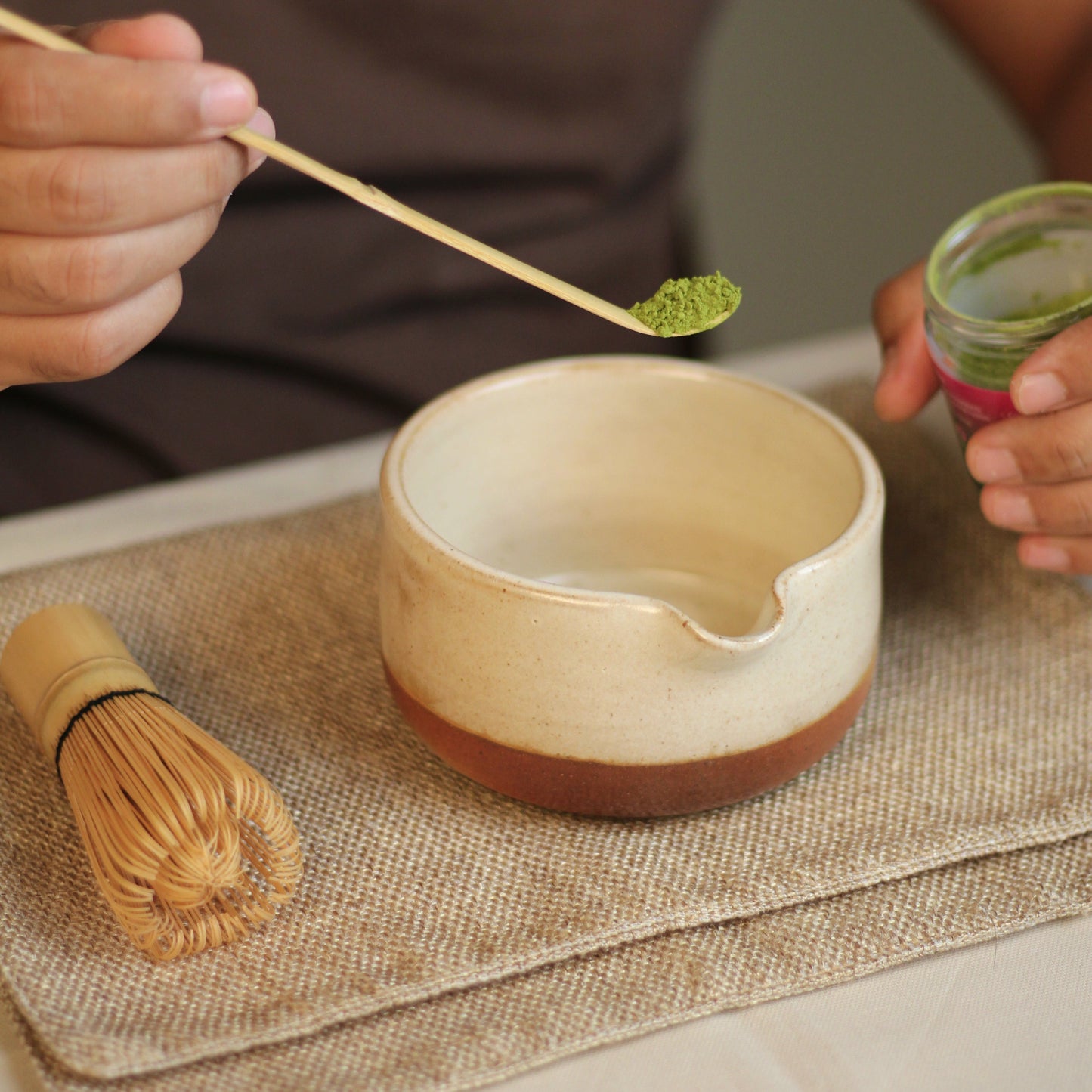 Person preparing matcha with a bowl and whisk on a textured surface
