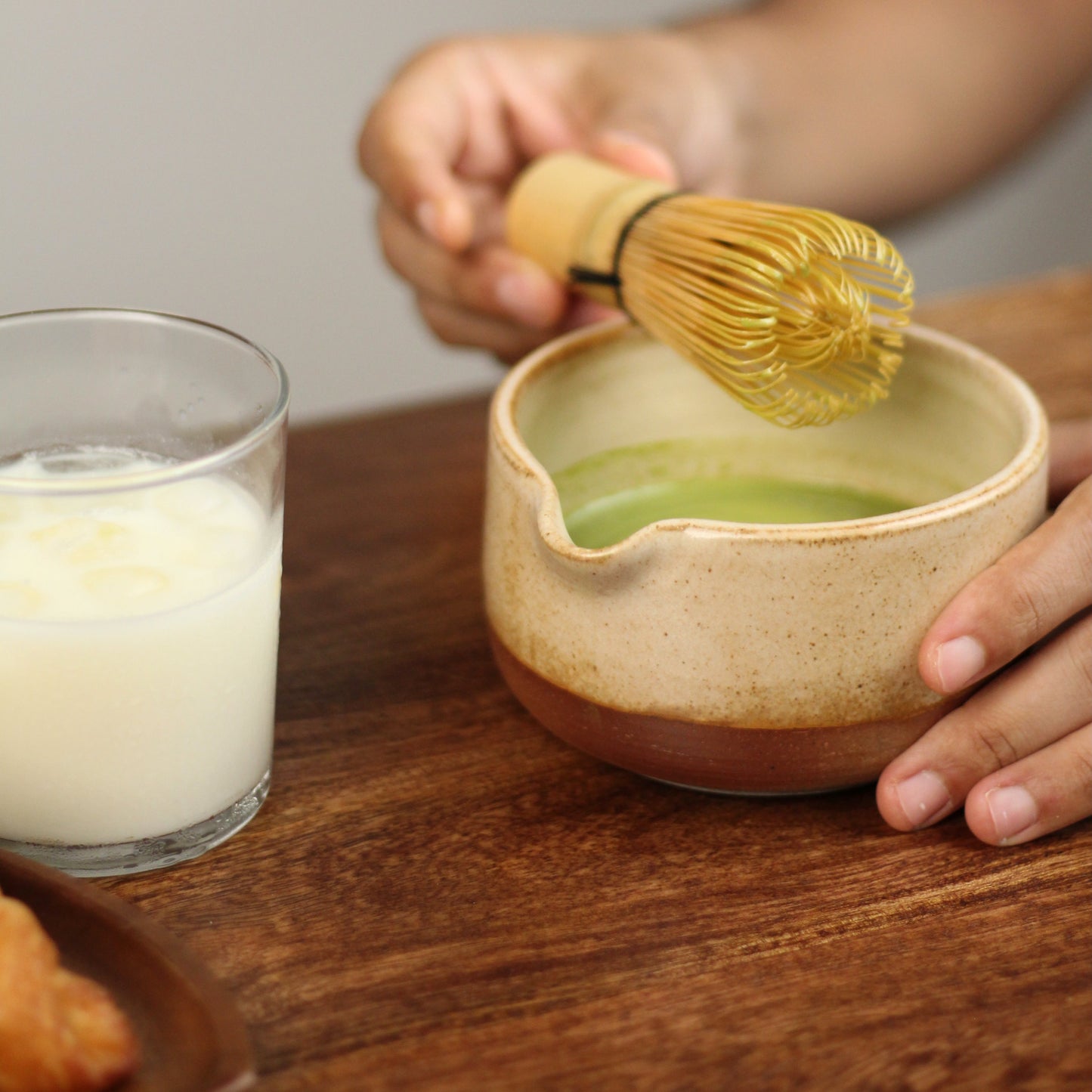 Person using a whisk to mix matcha in a bowl on a wooden table.