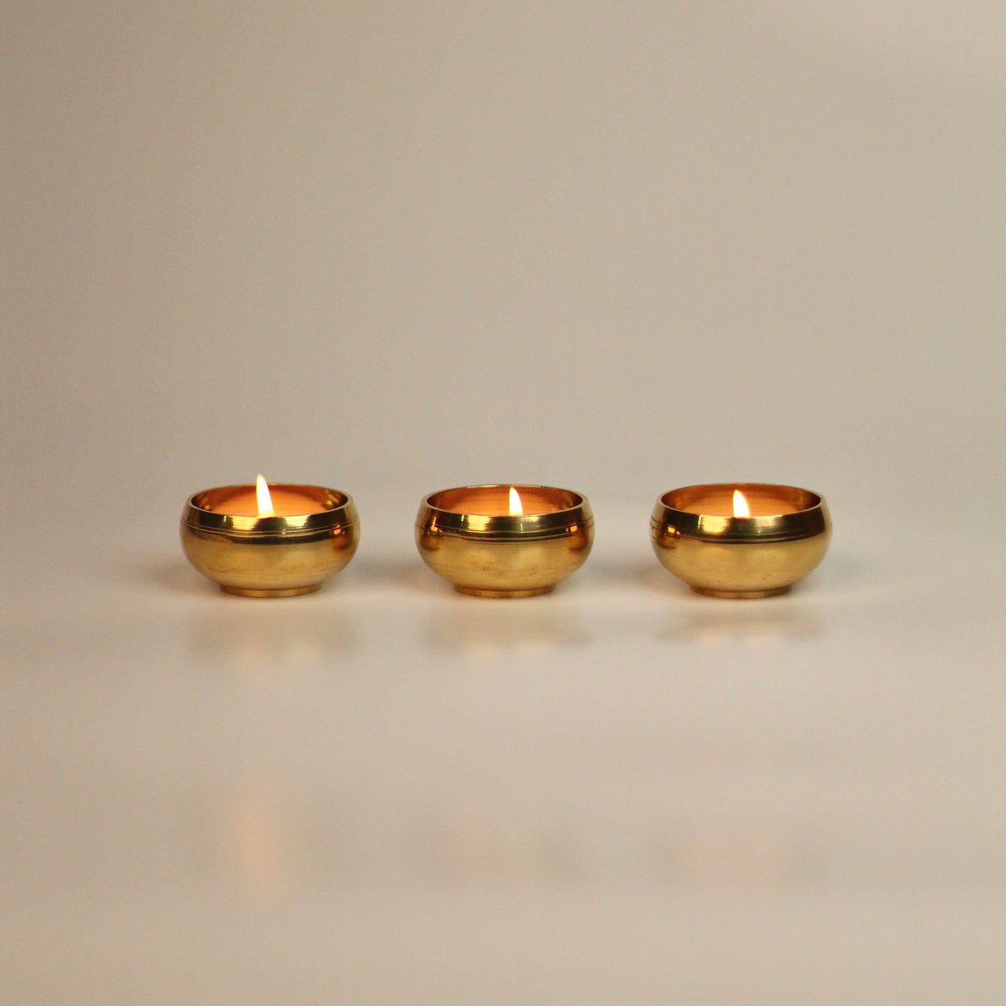 Three brass tealight holders on a beige background