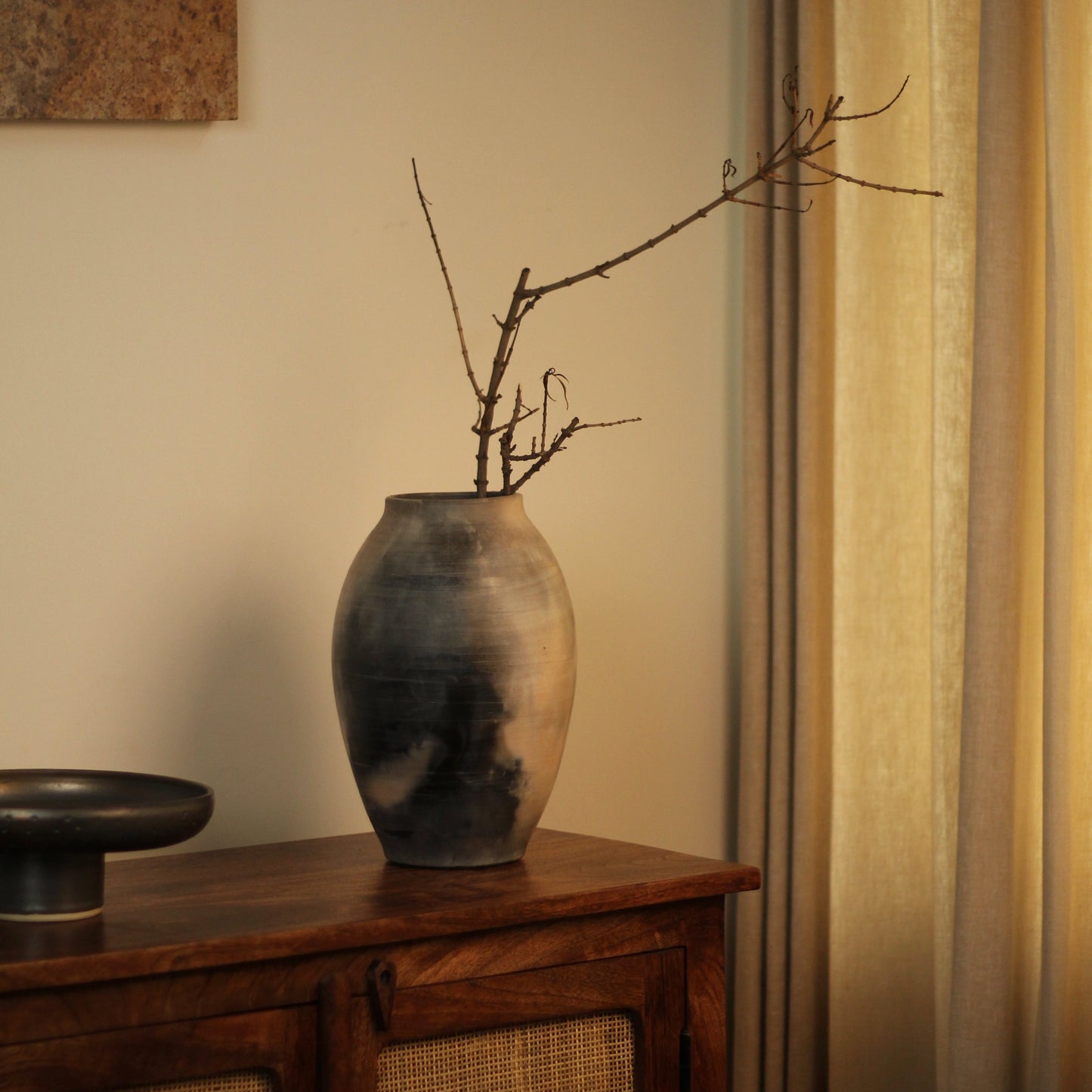 Kaari vase with branches on a wooden console table next to a curtain