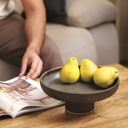 Three pears on a ceramic pedestal stand with a person and magazine in the background