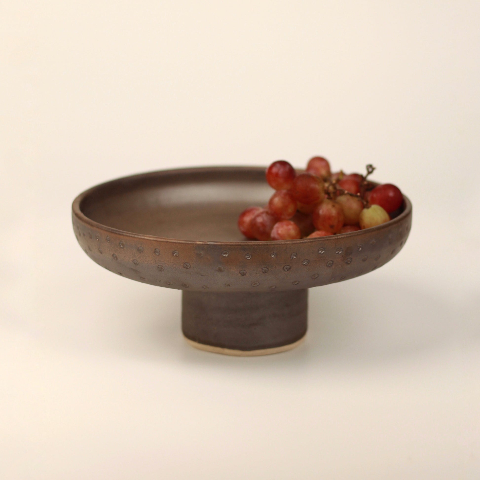 Pedestal bowl holding grapes placed on a neutral background