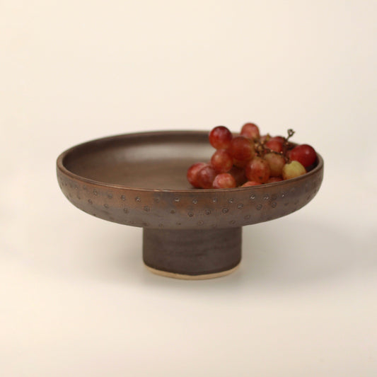 Pedestal bowl holding grapes placed on a neutral background