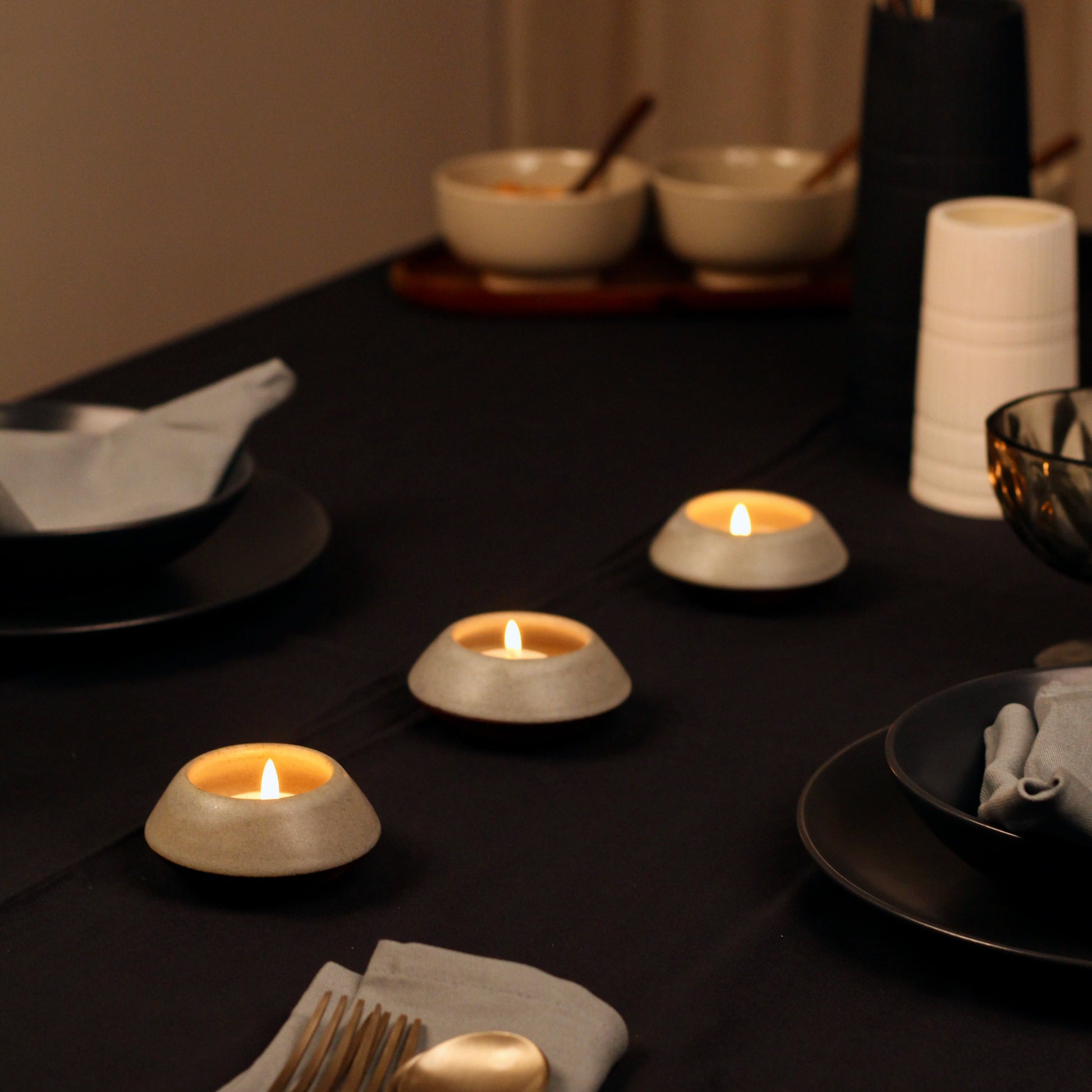 Dining table setting with candles, plates, and cutlery in a warm ambiance.