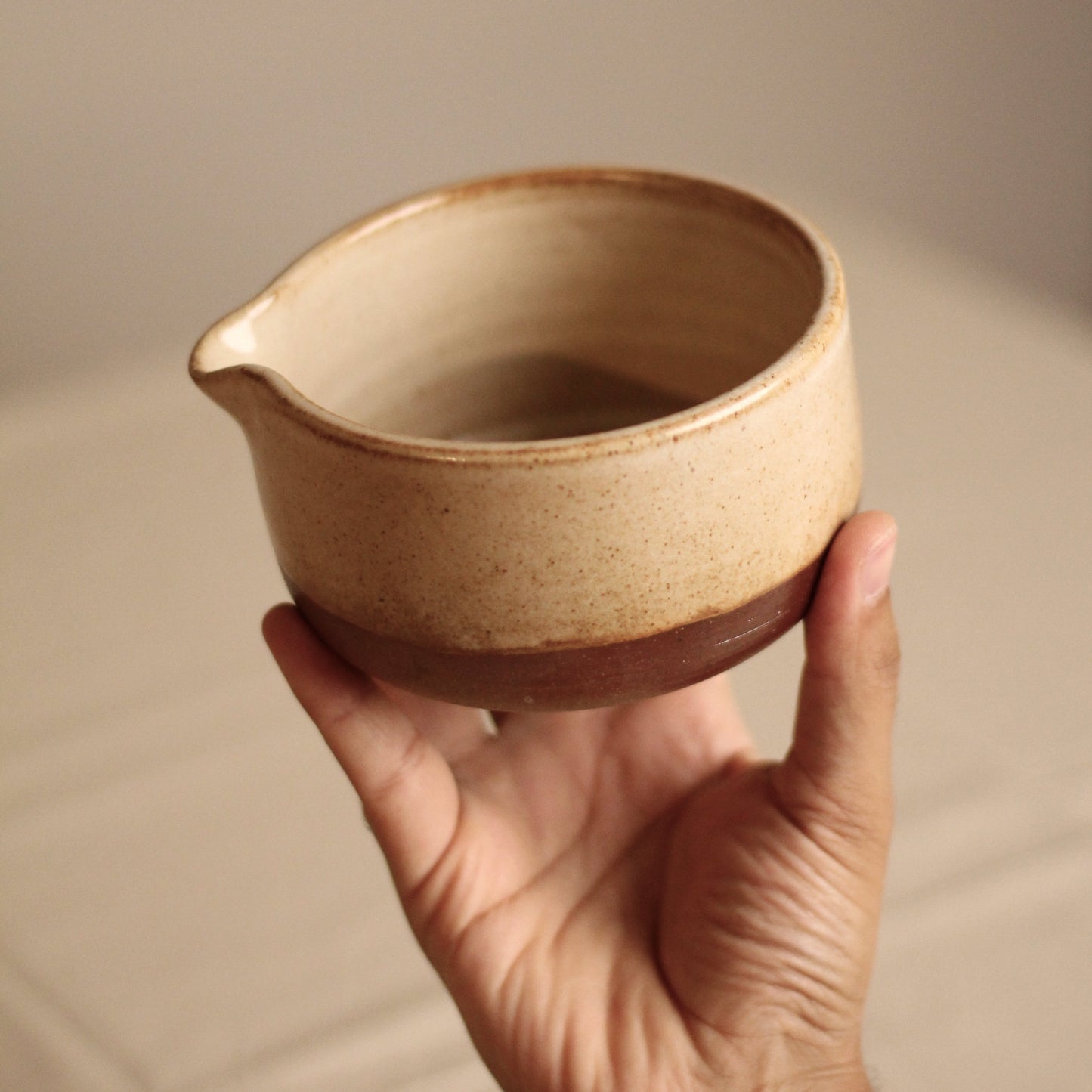 Hand holding a small matcha bowl against a neutral background