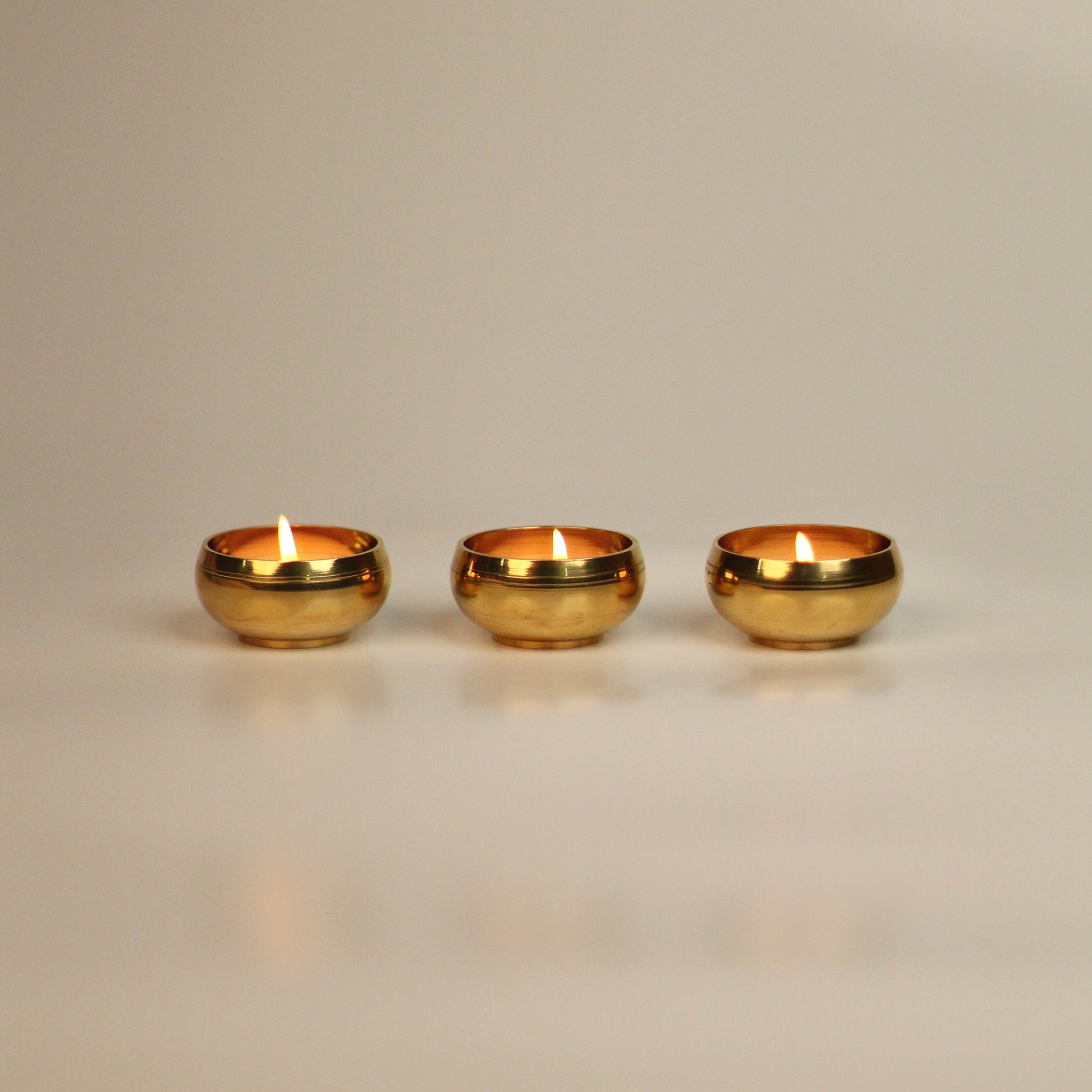 Three brass tealight holders on a beige background